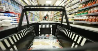 Cesta de compras vista de dentro, com prateleiras de produtos variados ao fundo em um supermercado.