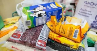 Caixa de leite, pacotes de feijão, farinha e macarrão empilhados em mesa.