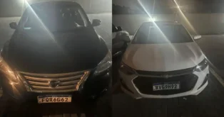 Dois carros estacionados em um estacionamento à noite, um preto e um branco, com placas visíveis.