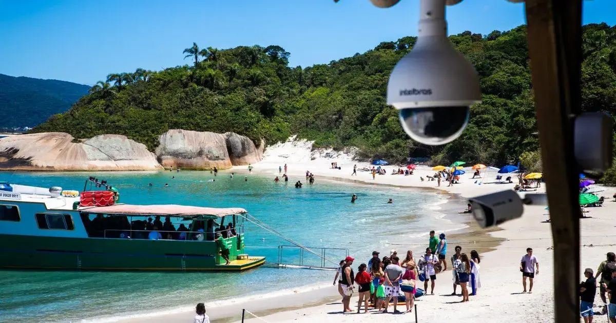 Barco de transporte atracado em uma praia com pessoas curtindo o sol e a água, cercado por vegetação.