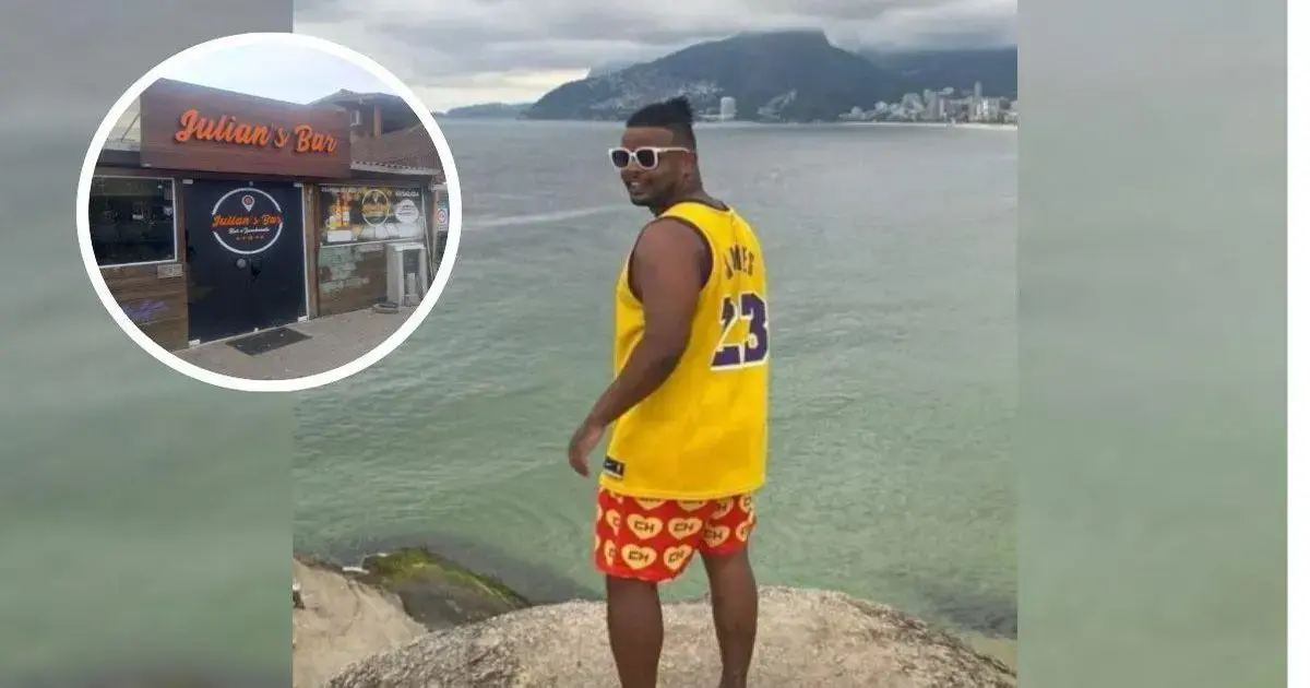 Homem de costas, usando camiseta amarelo com número 23 e shorts coloridos, posando em rochas à beira-mar.