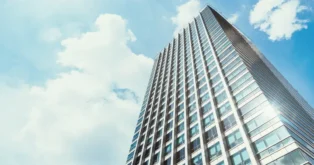 Edifício de estrutura moderna é visto de baixo, com céu azul e nuvens ao fundo.