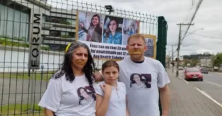 Mulher, menina e homem em frente a um fórum, com camisetas estampadas e cartaz sobre Ana Beatriz Schelter.