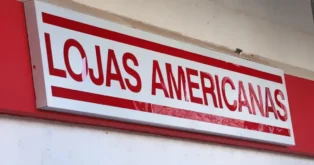 Placa com o nome "Lojas Americanas" em fundo vermelho, visível em um ambiente comercial.