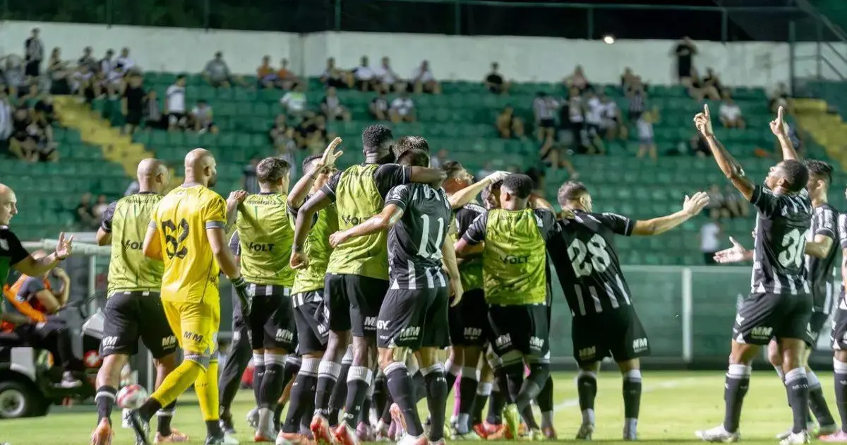 Jogadores celebrando juntos após um gol, com torcedores ao fundo em um estádio.