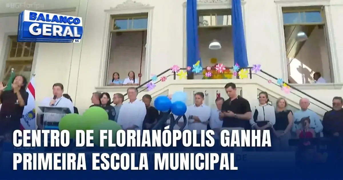 Centro de Florianópolis com faixa decorativa e grupo de pessoas em evento de inauguração da primeira escola municipal.