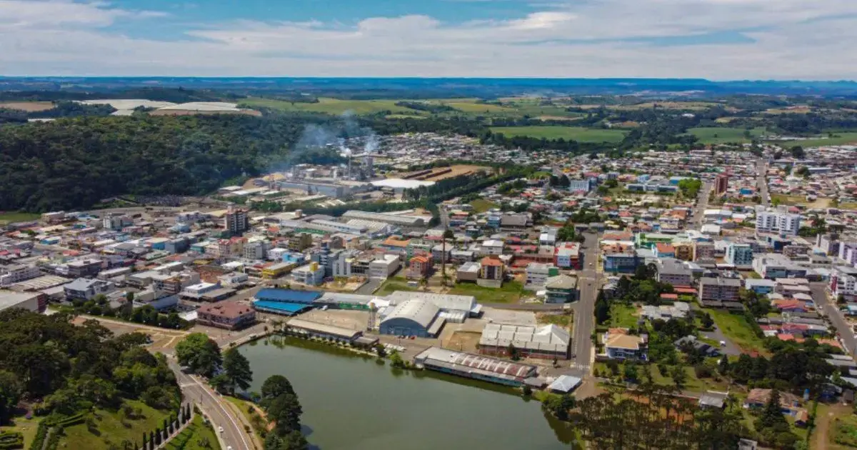 Vista aérea de uma cidade, com edificações, uma área industrial e um lago em primeiro plano.