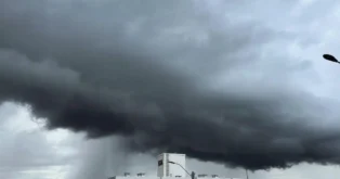 Nuvens escuras e densas em um céu nublado, com um prédio visível na parte inferior da imagem.