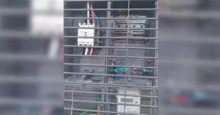 Painel elétrico com fiações expostas, dispositivos de proteção e medidor de energia visível na parte inferior.