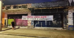 Faixa pendurada em prédio abandonado com a frase "Zona Livre para uso de crack e vadiagem" visível.