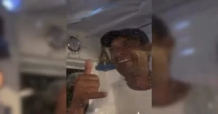 Homem sorridente fazendo sinal de positivo, com fundo de cabine de embarcação e alguns relógios visíveis.