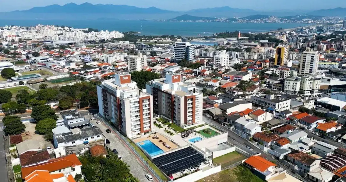 Vista aérea de um bairro com prédios, casas, ruas e áreas verdes, próximo ao mar.