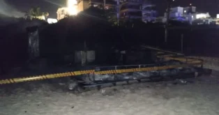 Quiosque queimado na Praia Grande, com estrutura destruída e cordão de isolamento visível.