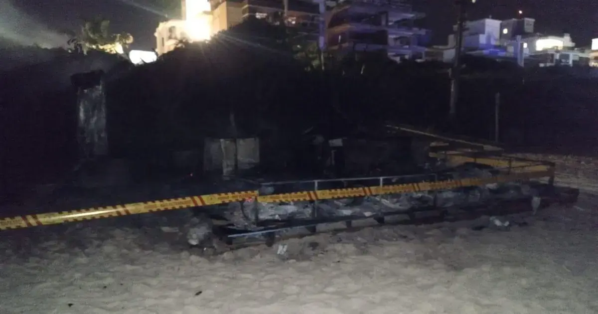 Quiosque queimado na Praia Grande, com estrutura destruída e cordão de isolamento visível.