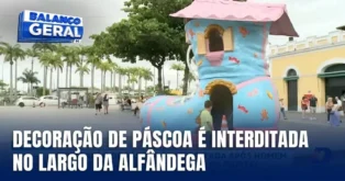 Decoração de Páscoa em forma de casa colorida interditada no Largo da Alfândega, cercada por pessoas e palmeiras.