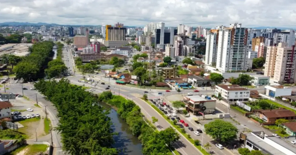 Vista aérea de uma área urbana com edifícios altos, ruas e vegetação em um dia ensolarado.