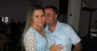 Casal posando para a foto em um ambiente interno, com música visível ao fundo.