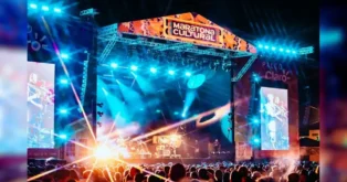 Palco iluminado da Maratona Cultural com pessoas assistindo ao show e projeções em telões.