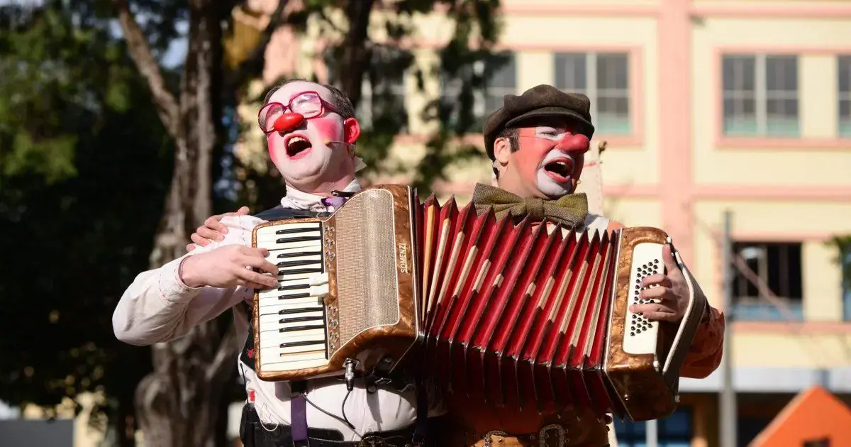 Dois palhaços cantando e tocando acordeões em uma apresentação ao ar livre.