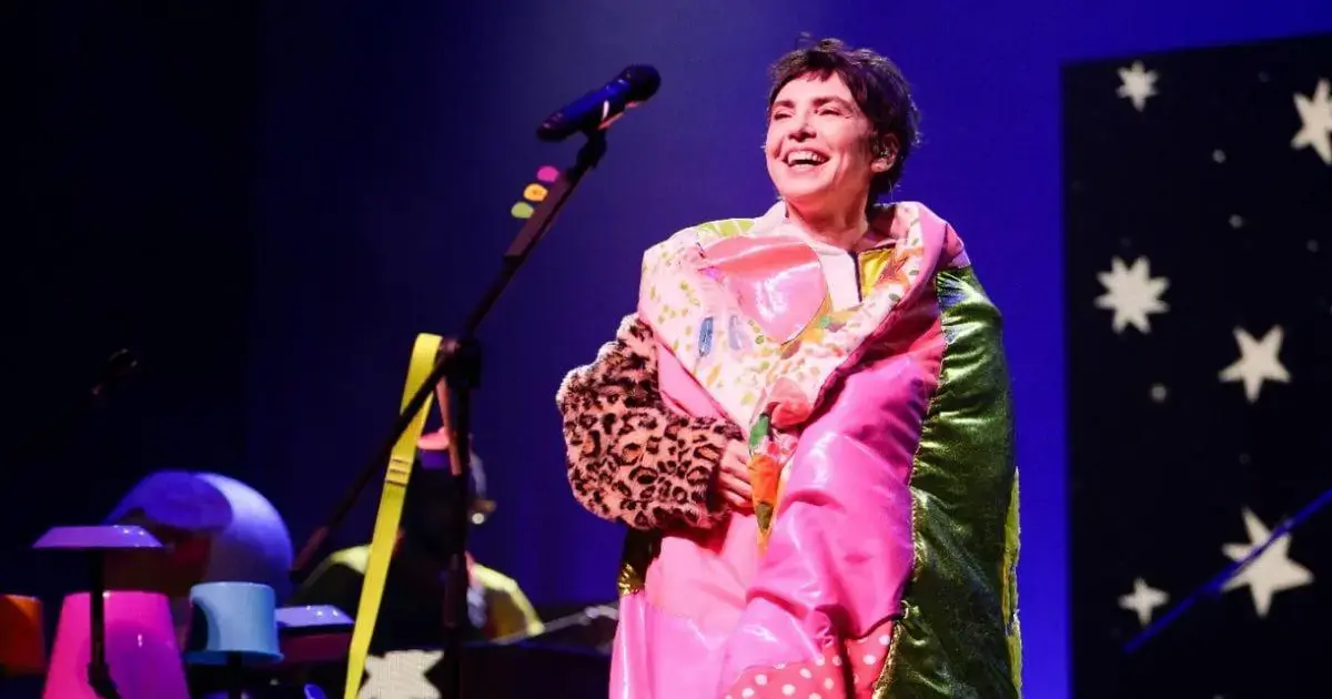 Performance de artista vestindo um traje colorido e divertido em um palco iluminado.