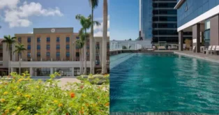 Edifício com relógio na fachada e piscina ao ar livre, rodeado por palmeiras e flores.