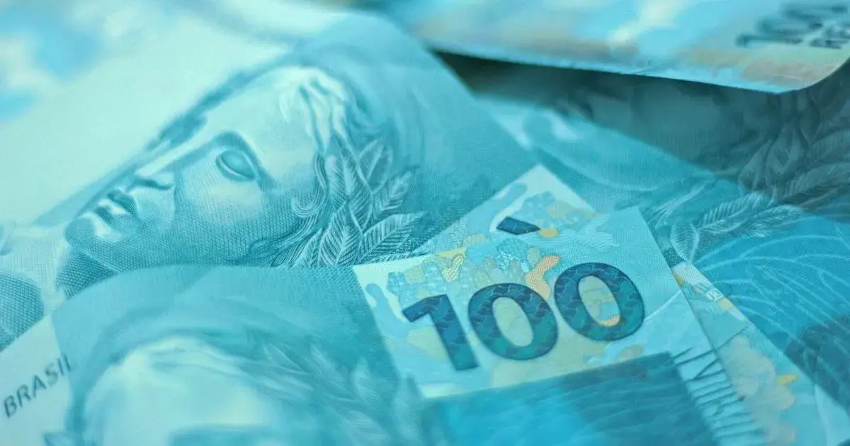 Notas de dinheiro em tons de azul, com destaque para a nota de R$ 100.