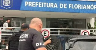 Placa da Prefeitura de Florianópolis ao fundo, com pessoas e policiais civis em primeiro plano.