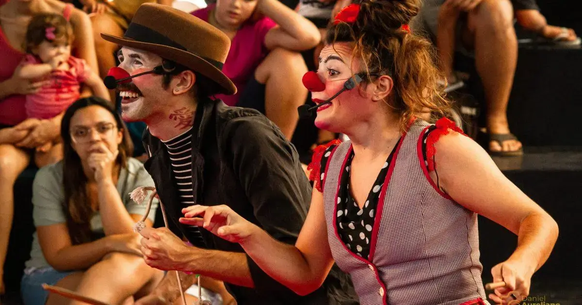 Artistas de palhaçaria interagindo com a plateia em um espetáculo, com expressão alegre e trajes coloridos.