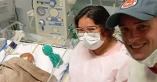 Mulher e homem sorrindo em um ambiente hospitalar, com um bebê em um berço ao fundo, cercado por equipamentos médicos.