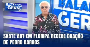 Apresentador em estúdio de TV, com camiseta colorida, anuncia doação para a exposição Skate Art em Florianópolis.