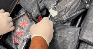 Mãos com luvas manipulando pacotes de droga, incluindo tabletes com bandeiras da Grã-Bretanha.