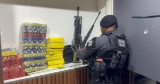 Militar inspecionando armamento ao lado de pacotes de drogas em um ambiente controlado.