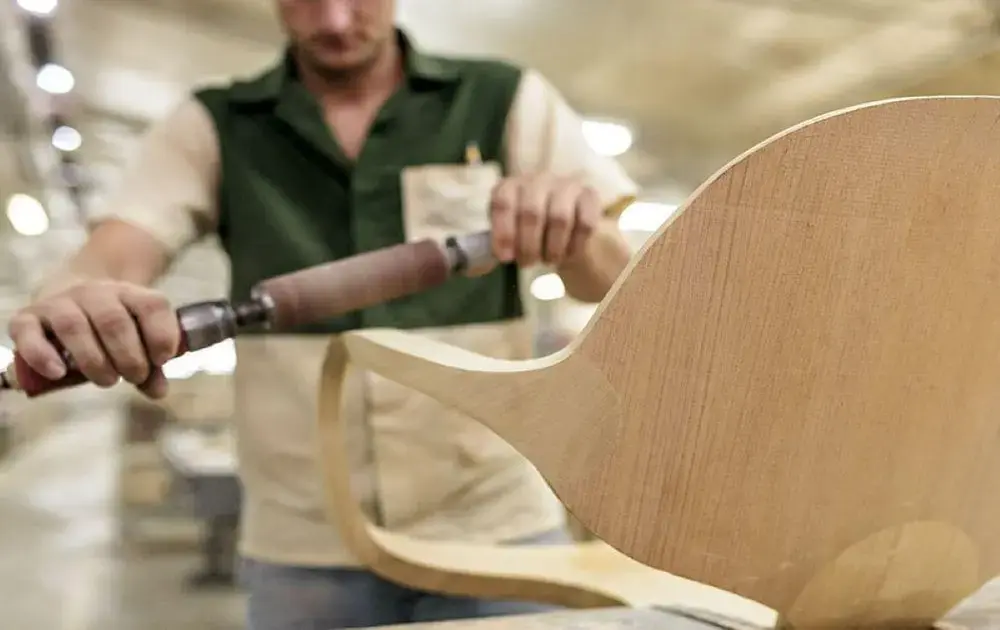 Indivíduo operando uma ferramenta elétrica para moldar madeira em uma oficina, com peça em destaque.