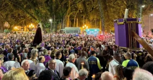 Multidão reunida durante procissão à noite, com pessoas usando vestes roxas e segurando velas.
