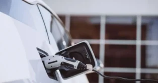 Porta de carregamento de um carro elétrico com cabo conectado, em fundo de claridade.