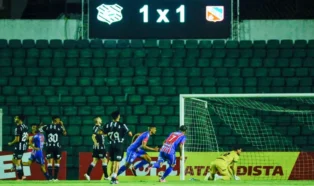 Placar de 1 a 1 iluminado no fundo, jogadores em campo celebrando e um goleiro no chão.