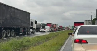 Congestionamento com diversos caminhões e carros em uma rodovia sob céu nublado.