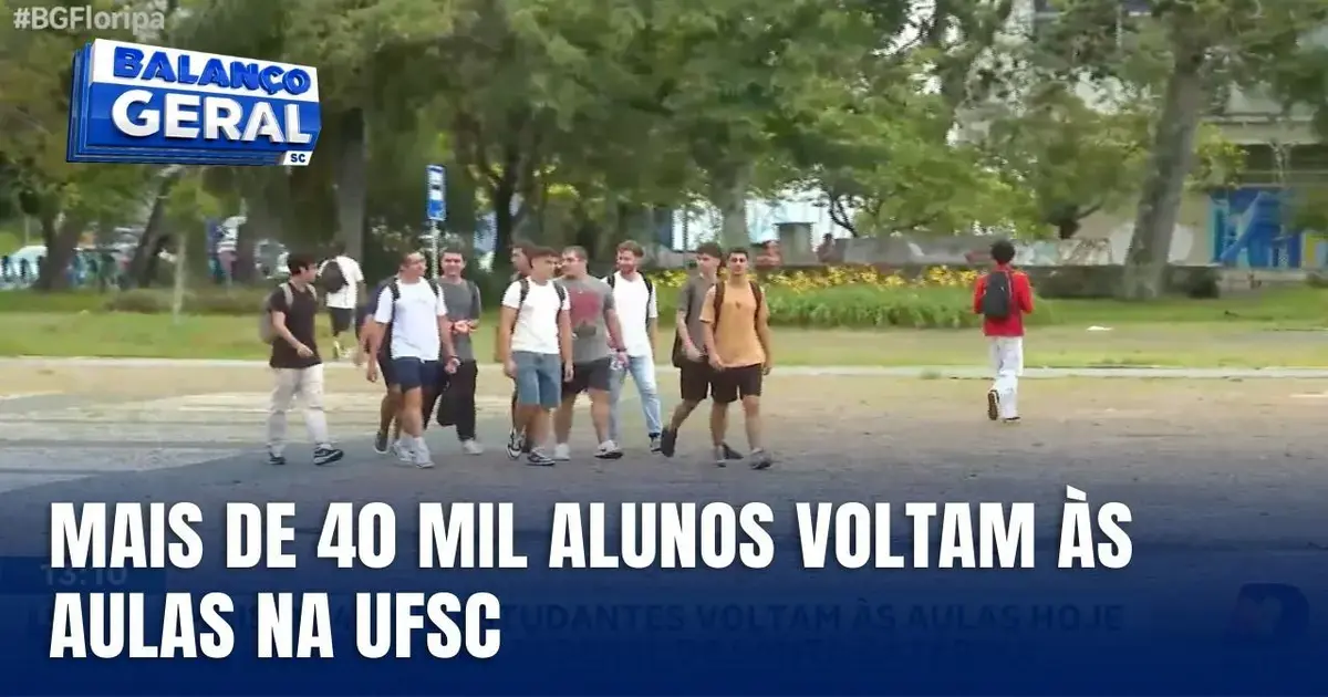 Grupo de estudantes caminhando em área externa da Universidade Federal de Santa Catarina, com árvores e prédios ao fundo.