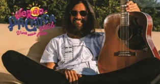 Homem sentado em um sofá, usando óculos escuros e segurando um violão, com uma camisa estampada. Texto em destaque acima.