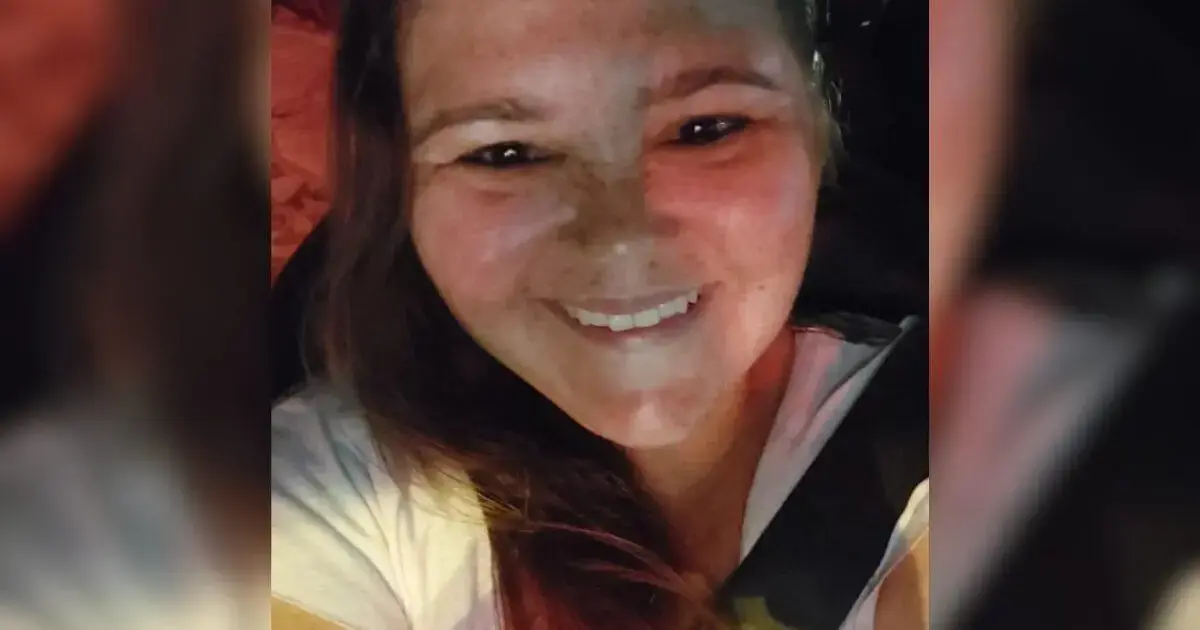 Retrato de uma pessoa sorridente com cabelo solto, usando uma camiseta clara e cinto de segurança, em um veículo.