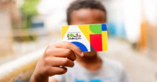 Criança segurando um cartão do programa Bolsa Família em ambiente urbano.