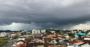 Céu nublado com nuvens escuras sobre uma área urbana, com prédios e casas visíveis.
