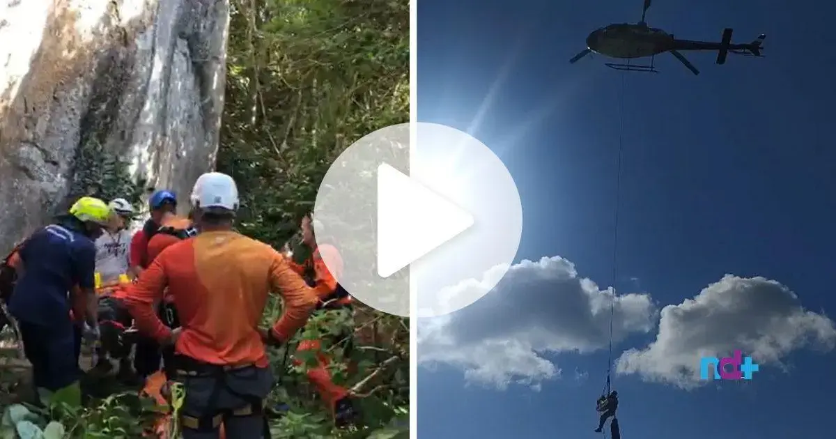 Grupo de pessoas em resgate, helicóptero com corda descendo em área de vegetação.