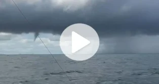 Um fenômeno meteorológico em alto-mar, com nuvens escuras e uma tromba d'água visível ao fundo.