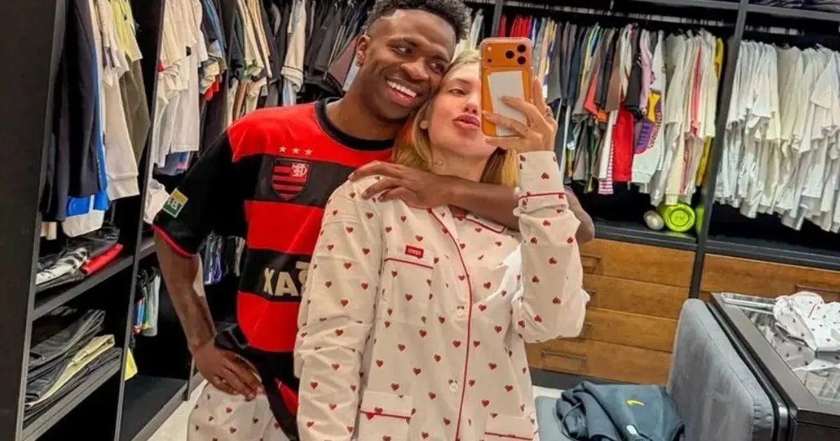 Casal tira selfie no closet, vestido com camisa de time e pijama com estampas de corações.