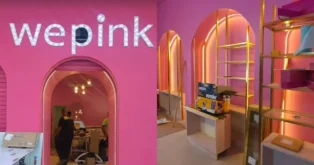 Letreiro iluminado "wepink" em uma parede rosa, com detalhes em iluminação laranja e móveis em andamento na loja.